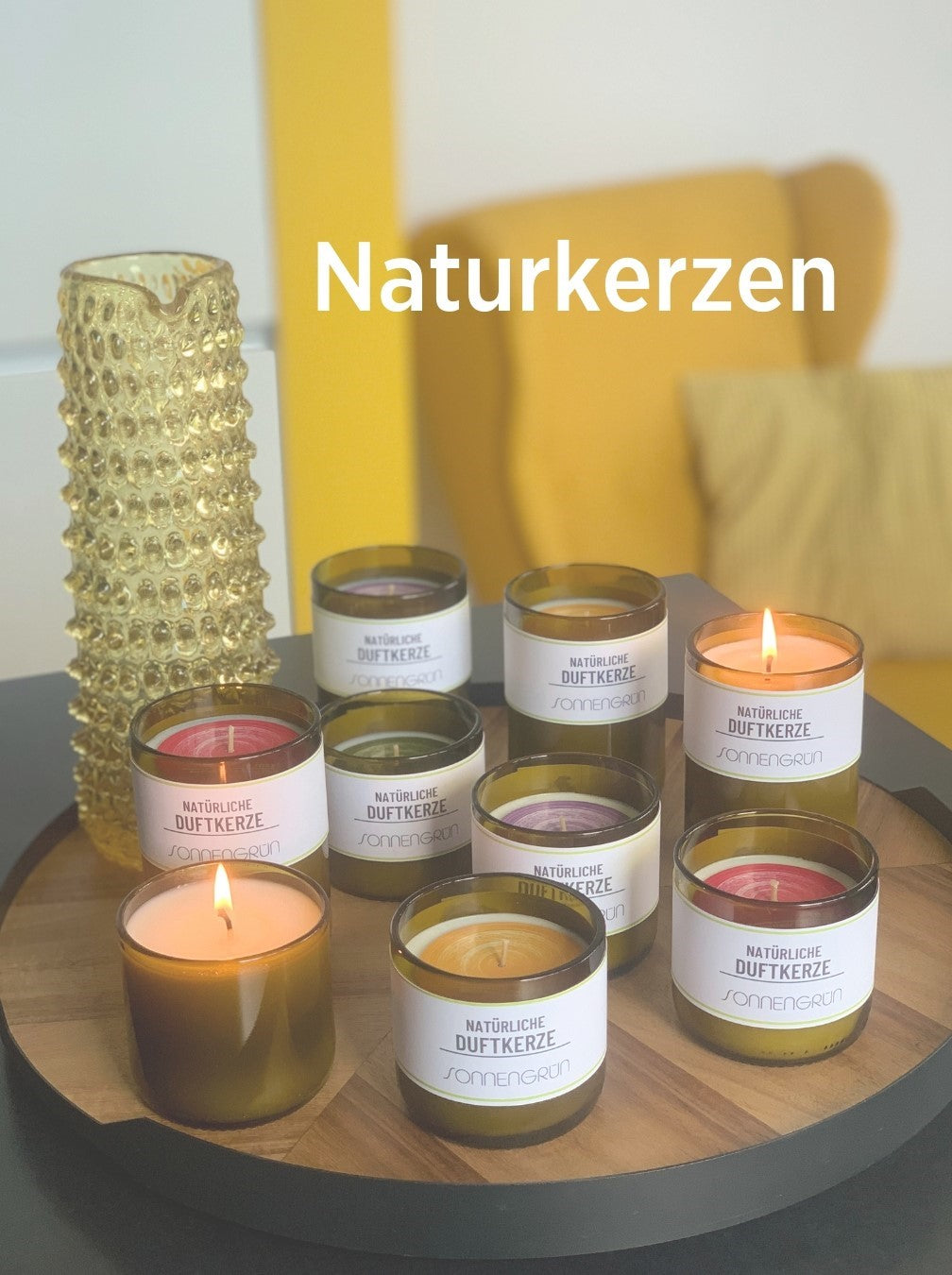 Auf diesem Foto sieht man die Duftkerzen von Sonnengrün auf einem Holztablett vor weißem Hintergrund mit gelbem Sessel. Als Dekoration sieht man ebenfalls einen gelben Glaskrug.