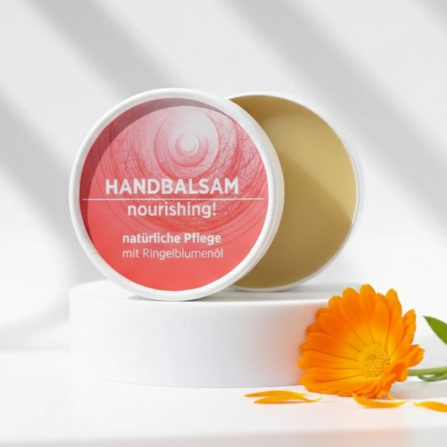 Handbalsam mit natürlichen Inhaltsstoffen für trockene Hände mit Ringelblume, Balsam ist in weißem, zylindrischem Karton verpackt mit rotem Etikett.