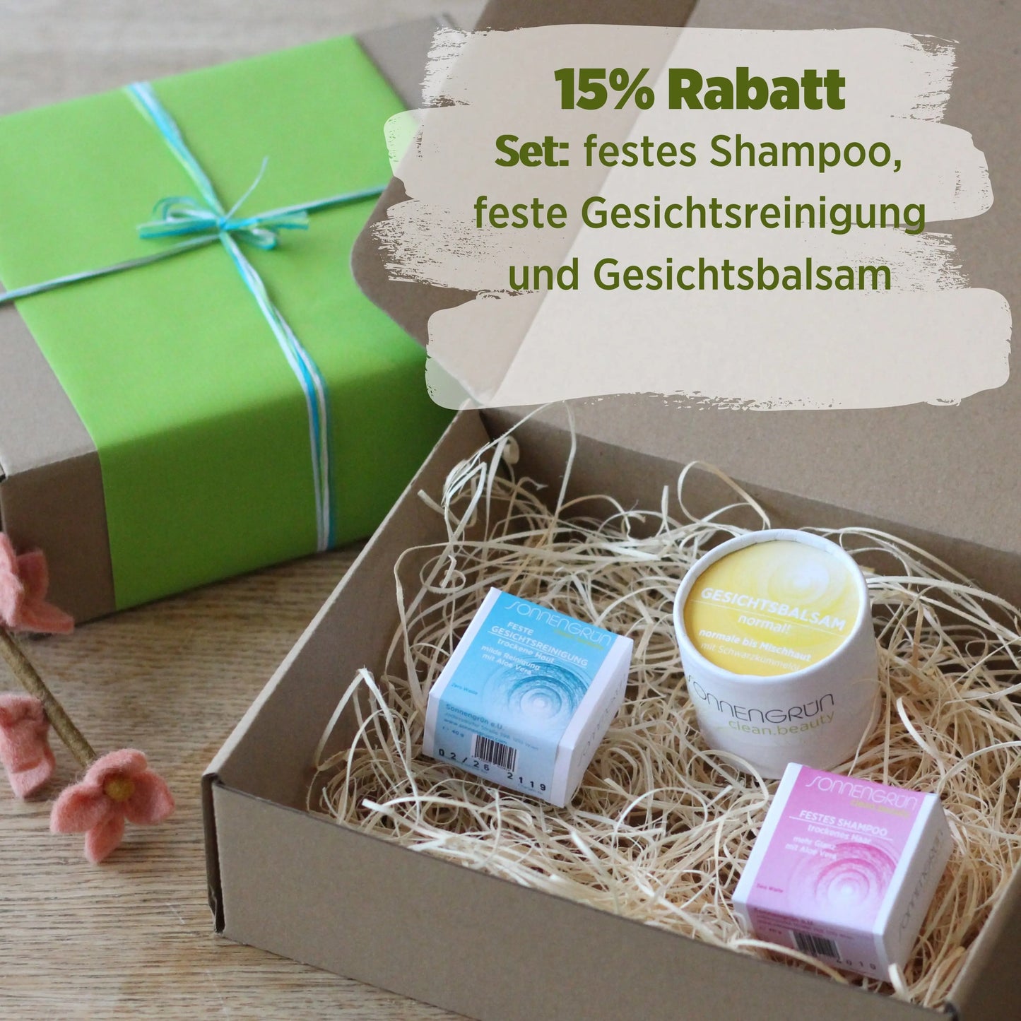 Auf diesem Bild sieht man einen beigen Karton mit den bunten Produkten von Sonnengrün darinnen. Im Hintergrund ist ein Geschenk mit grünem Geschenkpapier und Schleife.
