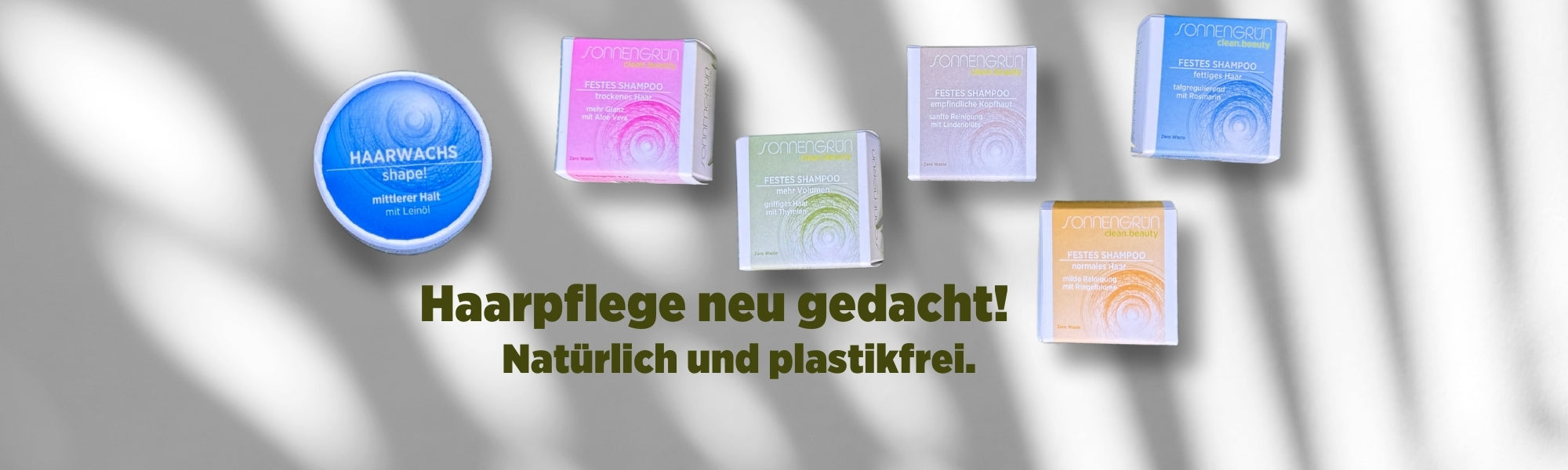 Auf dem Banner sieht man die bunt verpackten festen Shampoos und das Haarwachs von Sonnengrün in den farbigen Kartonagen Orange, Türkis, Grün, Blau und Schwarz vor einer weißen Wand mit Schattenspiel. Mit dunkelgrüner Schrift ist zu lesen "Haarpflege neu gedacht! Natürlich und plastikfrei."