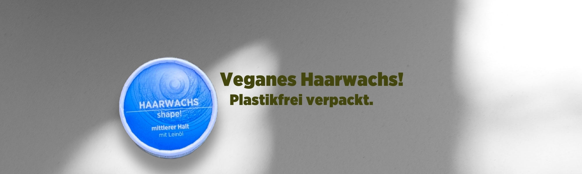 Auf dem Banner sieht man das bunt verpackte vegane Haarwachs von Sonnengrün mit blauem Etikett vor einer weißen Wand mit Schattenspiel. Mit dunkelgrüner Schrift ist zu lesen "Veganes Haarwachs! Plastikfrei verpackt."