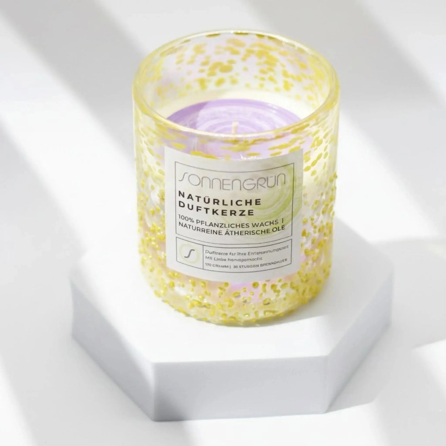 Auf diesem Foto sieht man die Duftkerze von Sonnengrün in einem gelben Glas auf einem weißen Podest stehen.