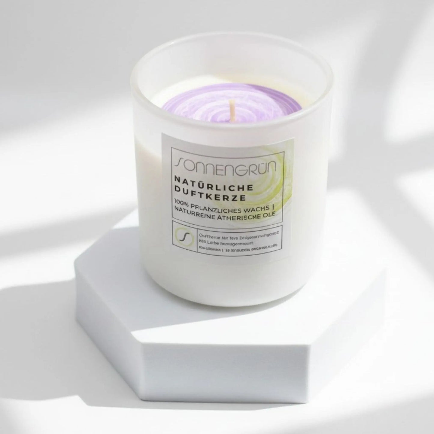 Auf diesem Foto sieht man die Duftkerze von Sonnengrün in einem weißen Glas auf einem weißen Podest stehen.