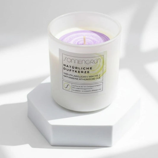 Auf diesem Foto sieht man die Duftkerze von Sonnengrün in einem weißen Glas auf einem weißen Podest stehen.