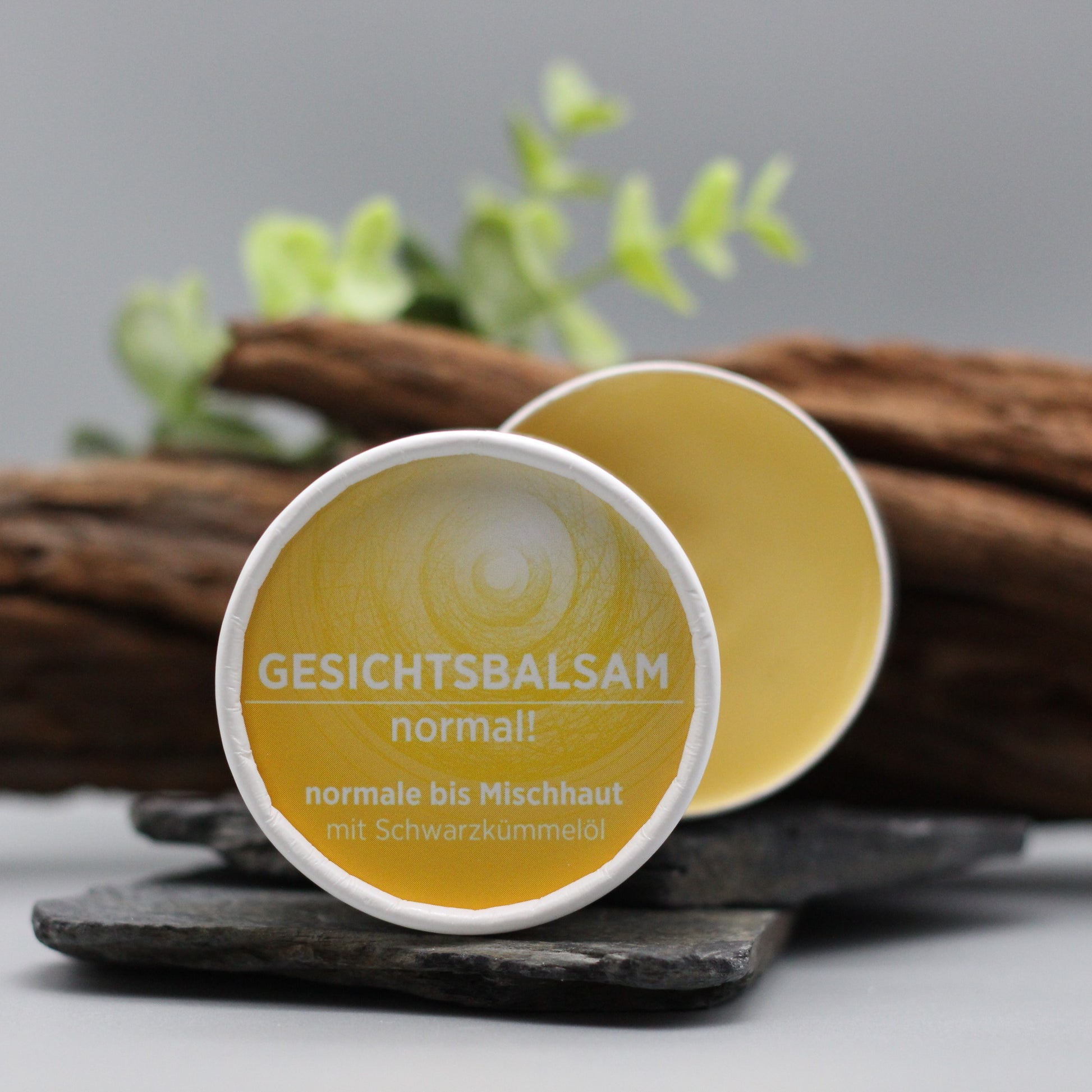 Gesichtsbalsam mit natürlichen Inhaltsstoffen für normale Haut mit Schwarzkümmelöl, Gesichtsbalsam ist in weißem, zylindrischem Karton verpackt mit gelbem Etikett.