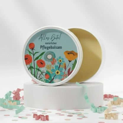 Auf dem Bild sieht man den Pflegebalsam mit einem Etikett, gestaltet speziell für Geburtstage. Auf dem Etikett sich man bunte Blumen abgebildet und die Aufschrift "Alles Gute!" und "natürlicher Pflegebalsam". Das Etikett macht den Körperbalsam zum perfekten Geburtstagsgeschenk.