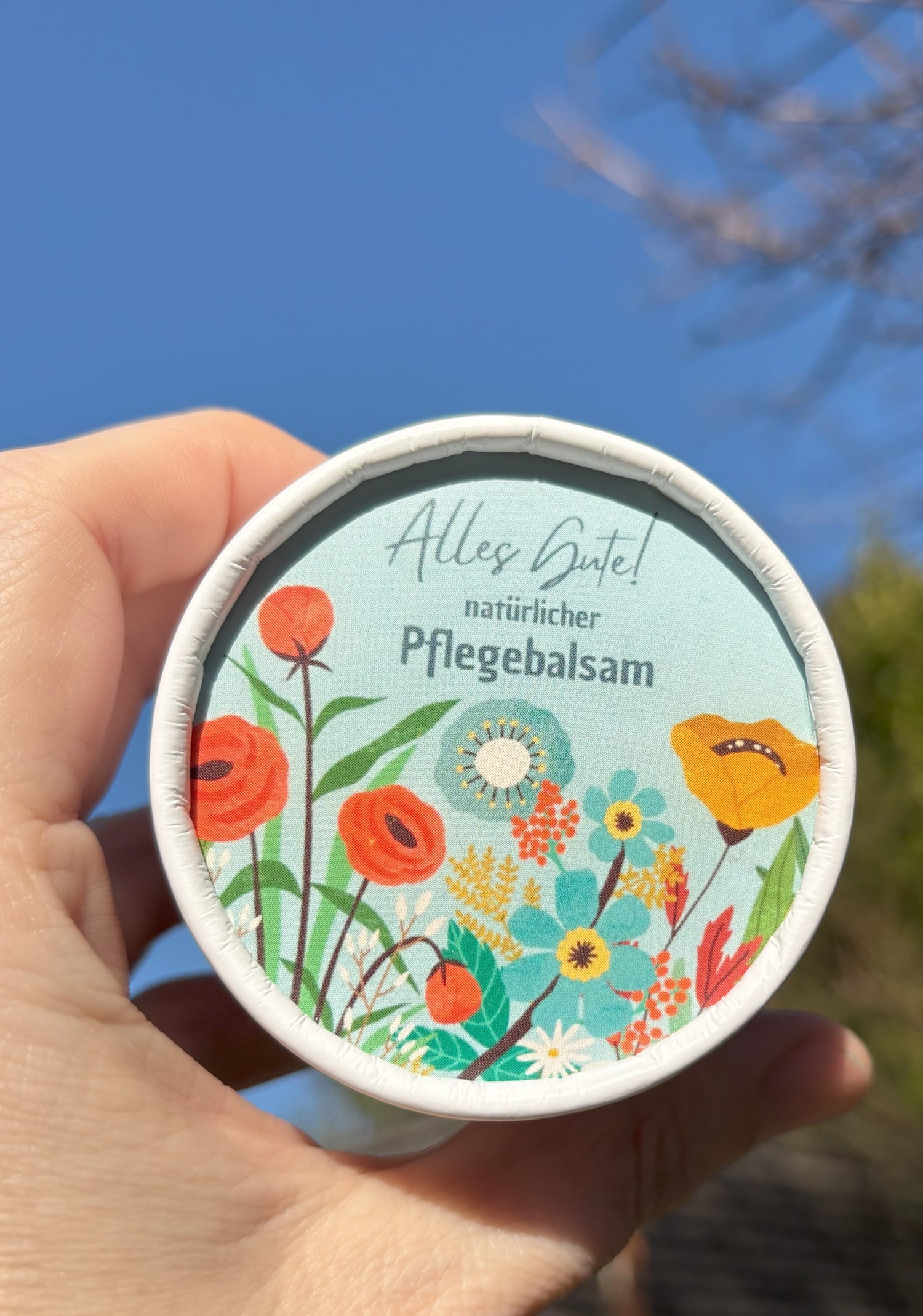Auf dem Bild sieht man einen Pflegebalsam von Sonnengrün mit einem individuellen Etikett. Auf dem Etikett sieht man Blumen und die Überschrift "Alles Gute!". Dieses Etikett kann über alle Pflegebalsame von Sonnengrün gelegt werden und mach somit die Zero Waste Kosmetik zum idealen Geschenk.