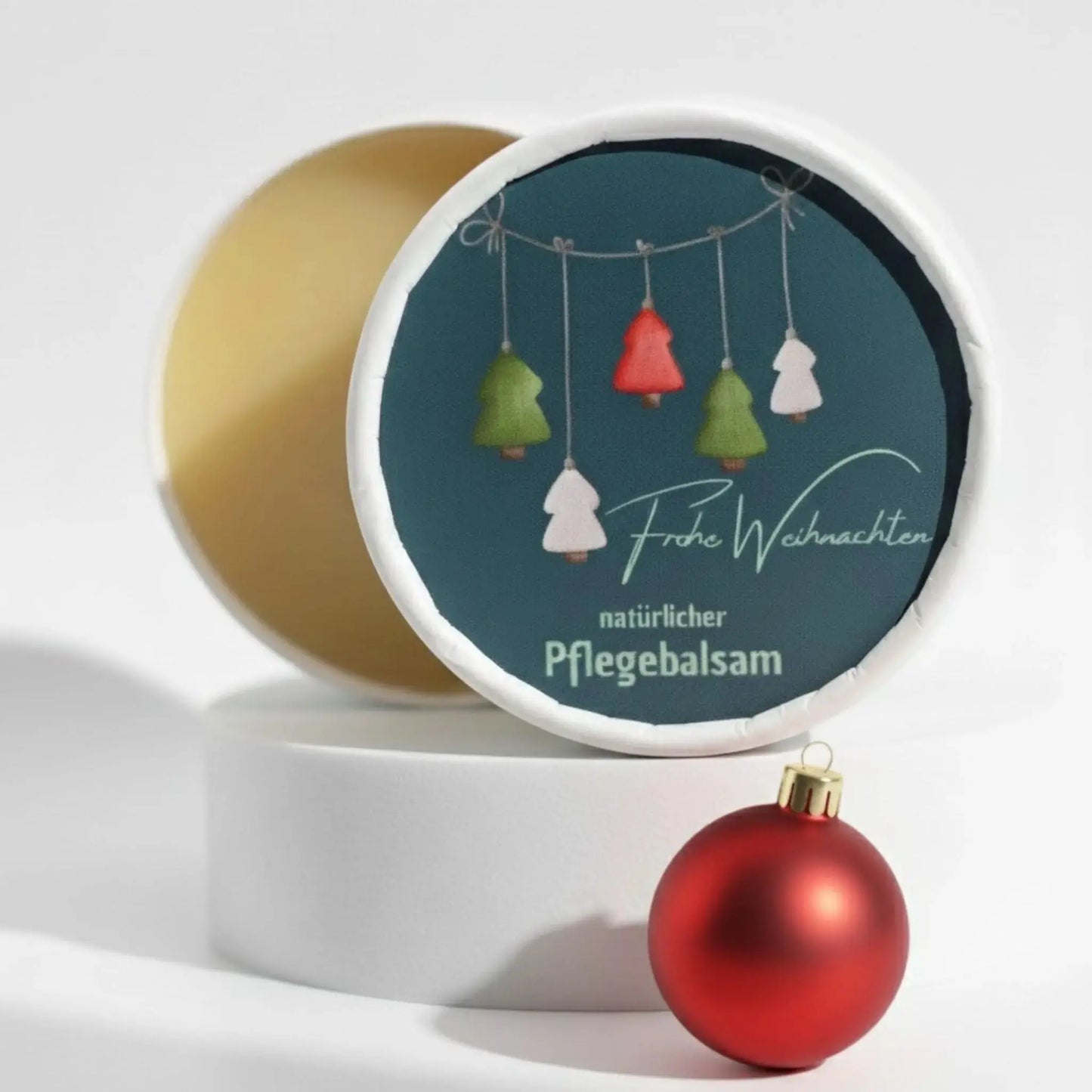 Auf dem Bild sieht man den Pflegebalsam mit einem Etikett, gestaltet speziell für Weihnachten. Auf dem Etikett sieht man ein weihnachtliches Motiv und die Aufschrift "Frohe Weihnachten!" und "natürlicher Pflegebalsam". Das Etikett macht den Pflegebalsam zum perfekten Weihnachtsgeschenk.