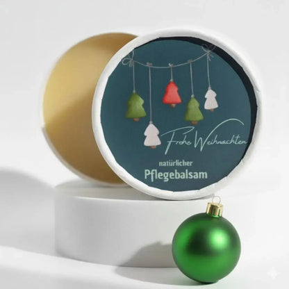 Auf dem Bild sieht man den Pflegebalsam mit einem Etikett, gestaltet speziell für Weihnachten. Auf dem Etikett sieht man ein Weihnachtsmotiv abgebildet und die Aufschrift "Frohe Weihnachten" und "natürlicher Pflegebalsam". Das Etikett macht den Körperbalsam zum perfekten Weihnachtsgeschenk.