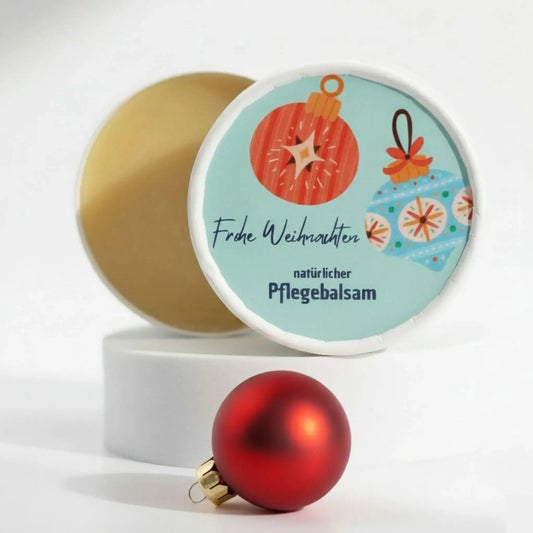 Auf dem Bild sieht man den Pflegebalsam mit einem Etikett, gestaltet speziell für Weihnachten. Auf dem Etikett sieht man ein weihnachtliches Motiv und die Aufschrift "Frohe Weihnachten!" und "natürlicher Pflegebalsam". Das Etikett macht den Pflegebalsam zum perfekten Weihnachtsgeschenk.