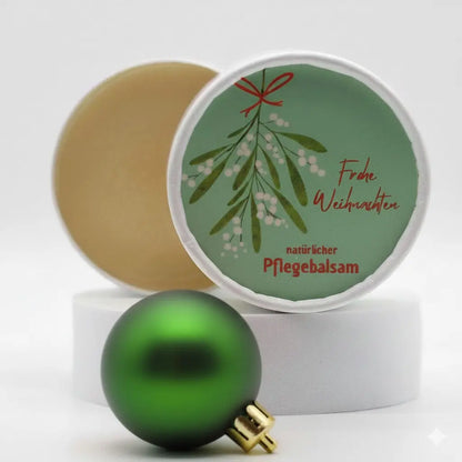Auf dem Bild sieht man den Pflegebalsam mit einem Etikett, gestaltet speziell für Weihnachten. Auf dem Etikett sieht man ein Weihnachtsmotiv abgebildet und die Aufschrift "Frohe Weihnachten" und "natürlicher Pflegebalsam". Das Etikett macht den Körperbalsam zum perfekten Weihnachtsgeschenk.