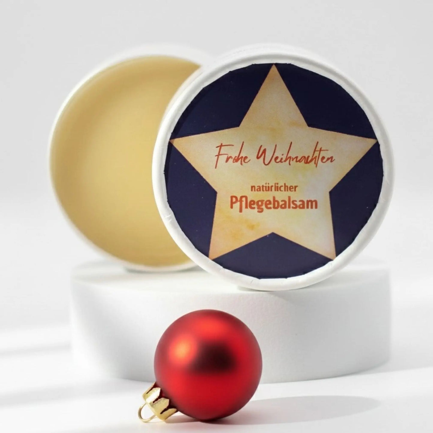Auf dem Bild sieht man den Pflegebalsam mit einem Etikett, gestaltet speziell für Weihnachten. Auf dem Etikett sieht man ein weihnachtliches Motiv und die Aufschrift "Frohe Weihnachten!" und "natürlicher Pflegebalsam". Das Etikett macht den Pflegebalsam zum perfekten Weihnachtsgeschenk.