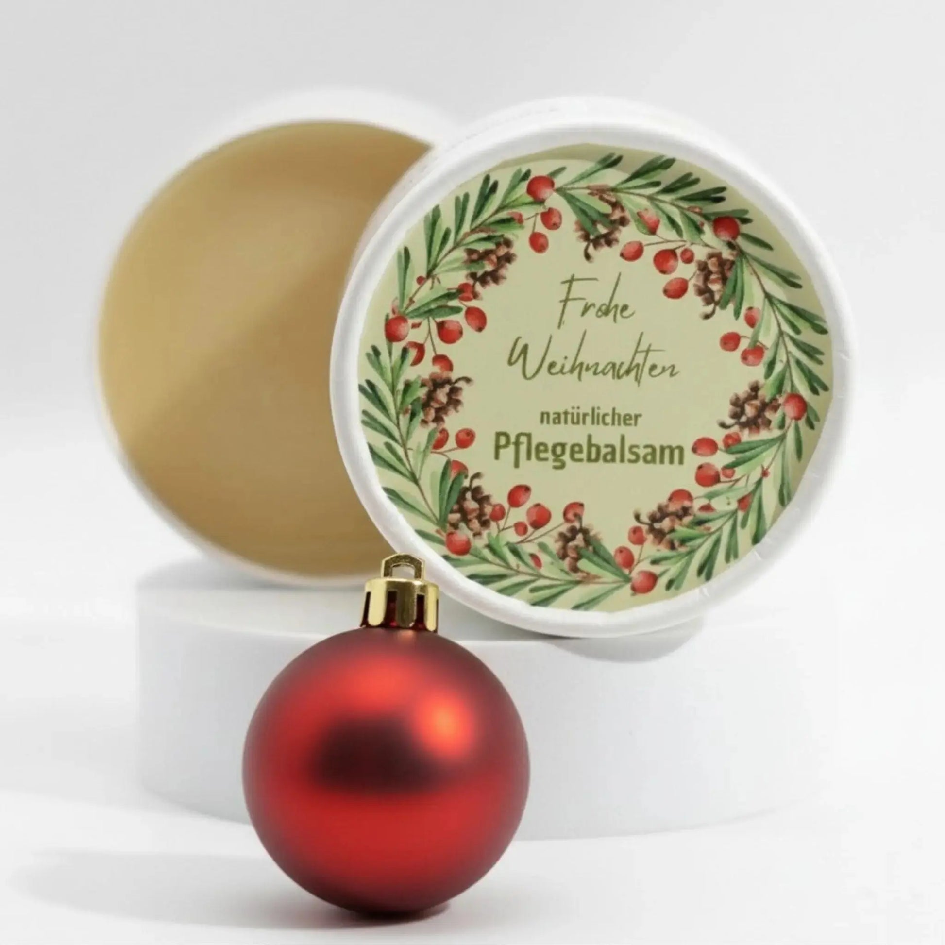 Auf dem Bild sieht man den Pflegebalsam mit einem Etikett, gestaltet speziell für Weihnachten. Auf dem Etikett sieht man ein weihnachtliches Motiv und die Aufschrift "Frohe Weihnachten!" und "natürlicher Pflegebalsam". Das Etikett macht den Pflegebalsam zum perfekten Weihnachtsgeschenk.