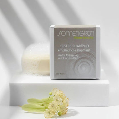 Auf dem Bild sieht man das runde feste Shampoo von Sonnengrün abgebildet. Es ist hinter der quadratischen Verpackung aus Karton mit beigen Etikett platziert. 
